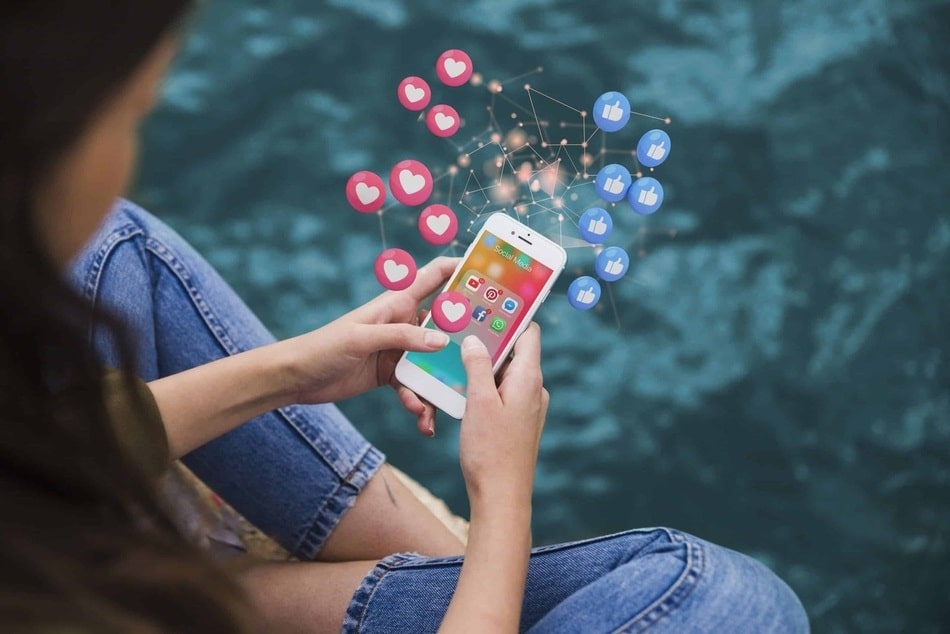 fotografia de mujer viendo sus redes sociales en un iphone, de la pantalla emergen simbolos de like y me gusta como efecto de animacion