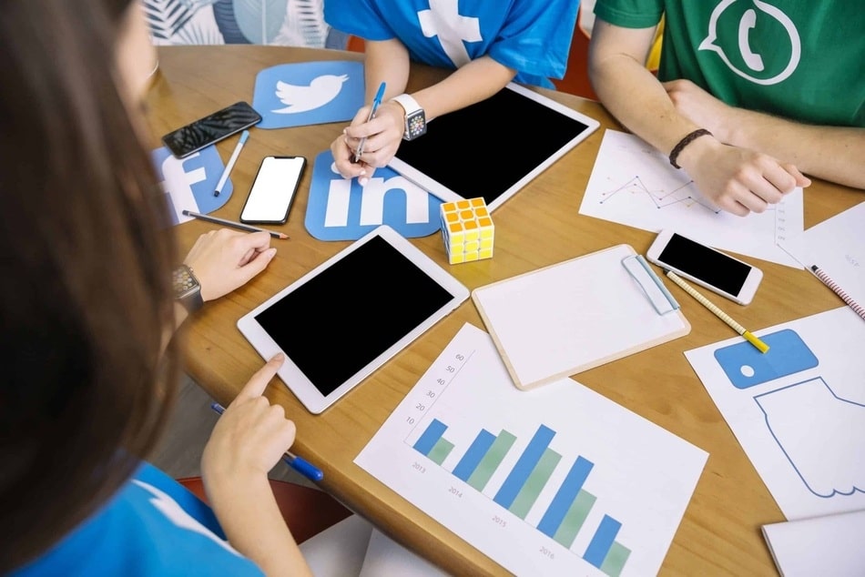 mesa de trabajo con personas expertas en marketing . Sobre la mesa hay graficas y estadisticas ejemplificando un servicio de gestion de redes sociales