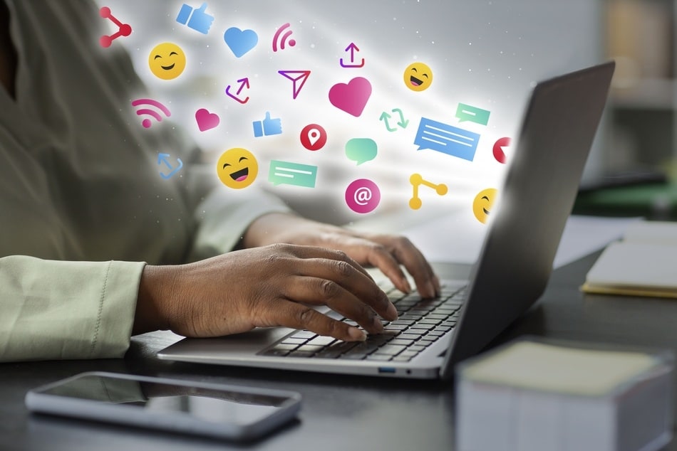 primer plano de una persona escribiendo en una computadora de donde emergen simbolos de redes sociales